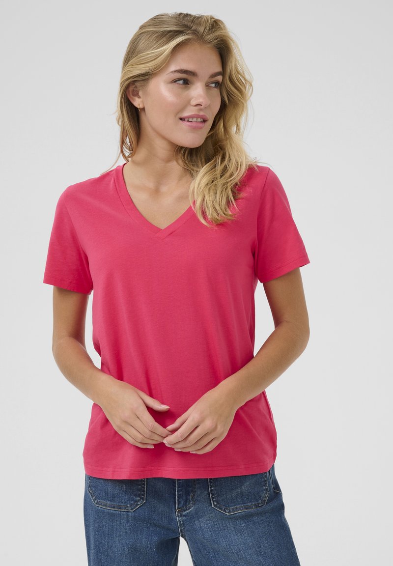 T-shirt fuchsia à col en V en tissu doux, doté de manches courtes et d'une coupe décontractée. Associé à un jean bleu foncé.