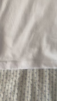 Tecido de algodão branco com uma textura suave, parcialmente drapeado sobre um tecido estampado com linhas e formas cinzas verticais.