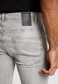 Grijze denim jeans met een zwart leren label "CARS" op de tailleband, met een ontwerp voor de achterzak en subtiele stikdetails.