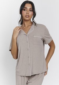 Camiseta de pijama de manga corta en tejido acanalado beige con ribete blanco, bolsillo frontal y cierre de botones. Textura suave, corte relajado.