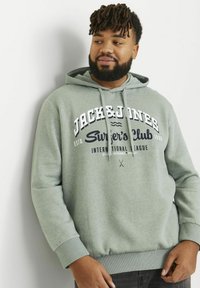 Sudadera verde con capucha, con un logo impreso en color marino. Puños y dobladillo acanalados, textura suave y un ajuste casual.