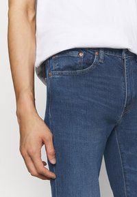 Mörkblå denimjeans med smal passform, utrustade med kopparfärgade detaljer, fem fickor och synliga sömnadsdetaljer på sömmarna.