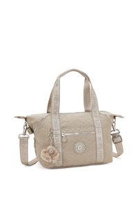Bolso Kipling beige con dos asas, correa de hombro desmontable, bolsillo con cremallera en la parte frontal y llavero de mono peludo colgando de la asa.