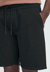 Zwarte sweatshorts van zachte stof, met een elastische tailleband met trekkoord, zijzakken en een schone, minimalistische uitstraling.