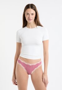 Biały top z krótkim rękawem w połączeniu z różowymi majtkami w paski, ozdobionymi koronką i małą kokardką na środku z przodu. Gładka tekstura na całej powierzchni.