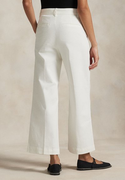 Białe spodnie szerokie z wysokim stanem, z tylnymi kieszeniami i gładką fakturą, w połączeniu z czarnymi butami wsuwanymi.