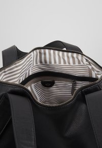 Černá taška na zip s texturovaným vnějškem; uvnitř má pruhovaný vzor v béžové a bílé barvě, se malou kapsou na zip.