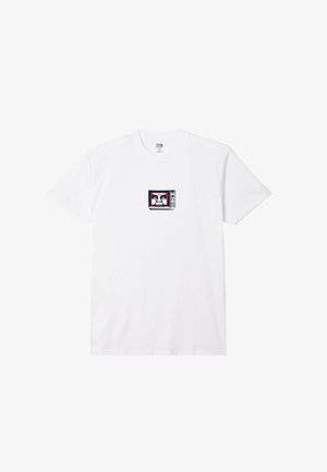 Camiseta de algodón blanca con un pequeño gráfico de un televisor vintage con un borde rojo y azul en el centro. Mangas cortas, cuello redondo.