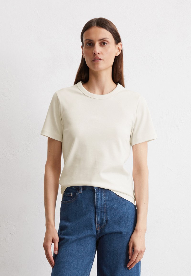 Cremfarbener Baumwoll-T-Shirt mit kurzen Ärmeln, Rundhalsausschnitt und lockerem Schnitt, kombiniert mit dunkelblauen Jeans.