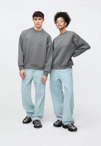 Grey oversized sweatshirts with dropped shoulders, paired with light blue wide-leg jeans. Sneakers complete the casual outfit. Minimalist design.