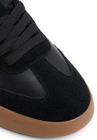 Zapatillas de ante y cuero negro con punta redondeada, parte superior texturizada y cordones oscuros. Presentan una suela de goma marrón.