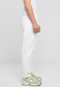 Joggers de algodón blancos con un corte relajado, que cuentan con una cintura con cordón, bolsillos frontales y un ligero desgaste en la tela.