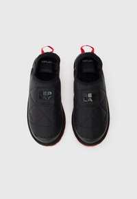 Zapatillas negras sin cordones con un upper texturizado de patrón diamante, parche con logo negro y acentos rojos en la suela y la pestaña de agarre.