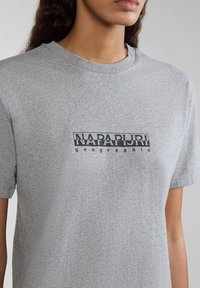 Harmaa puuvillainen t-paita lyhyillä hihoilla, jossa edessä mustalla värillä painatettu logo "NAPAPIJRI geographic". Pehmeä rakenne ja rento istuvuus.