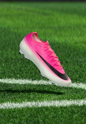 Chaussure de football rose vif avec logo de marque swoosh noir flottant au-dessus d'un terrain en herbe verte avec des lignes blanches.