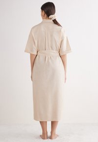 Beiges Leinenkleid mit kurzen Ärmeln, midi-langer Schnittführung und einem taillierten Gürtel. Es verfügt über eine Rückensattelnaht und einen lockeren Sitz mit minimaler Textur.