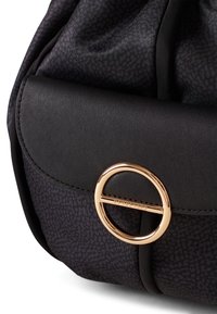 Czarna torba z tkaniny o teksturowanym wzorze, z gładką czarną klapą ze skóry i złotym okrągłym zapięciem.