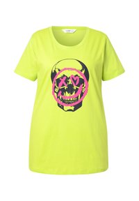 T-shirt en coton vert néon avec un graphique de crâne noir à l'intérieur d'un cercle rose, avec des yeux en forme de X et une bouche souriante. Manches courtes et col rond.