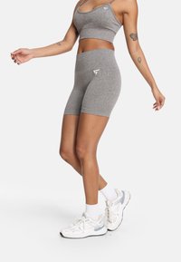 Sivé športové šortky s vysokým pásom a logom na boku, skombinované s hodícim sa crop topom a bielymi teniskami.