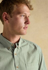 Zeleno-biely pruhovaný košeľový vrch s golierom, predným vreckom a perlovými gombíkmi s hladkým povrchom.