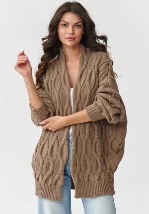 Brązowy sweter z dzianiny z teksturowanym wzorem w warkocze, otwarty z przodu, z luźnymi rękawami i ściągaczem na dole. Nosi się go na prostą bluzkę i dżinsy.