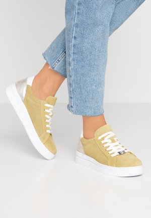 Lichtgele suède sneakers met witte veters en een metalen zilveren hieldetail, gedragen met kortere blauwe spijkerbroek.