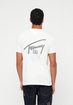 Biała koszulka bawełniana z niebieskim tekstem graficznym z tyłu, zawierająca nazwę "Tommy" i nazwy miast. Okrągły dekolt, krótki rękaw, luźny krój.