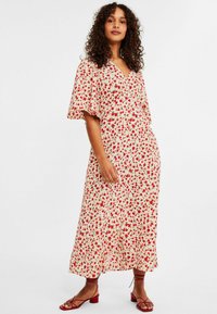 Blommig midiklänning i krämfärg med röda blommor, lös ärmdesign, V-ringning och lätt tyg. Matchad med röda sandaletter med remmar.