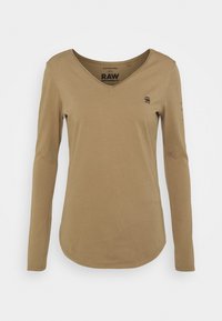 Långärmad brun V-ringad tröja med liten logotyp på bröstet och tryckt text på den inre kragen och vänster ärm på vit bakgrund.