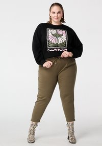 Zwarte sweatshirt met een bloemmotief in roze en groen; olijfgroene broek; grijze enkellaarsjes met slangenprint; casual pasvorm met ontspannen silhouet.