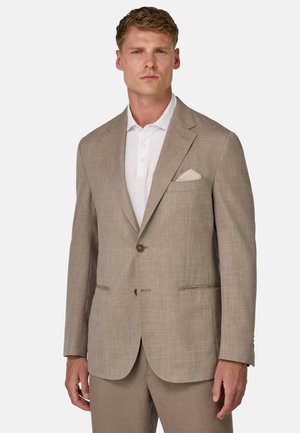 Blazer in lino beige con una camicia leggera sotto, chiusura a un bottone e fazzoletto da taschino. Presenta una texture liscia e un sottile motivo a intreccio.