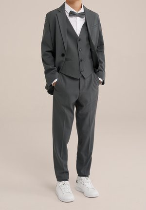 Szary garnitur składający się z trzech części, z kamizelką podwójnie zapinaną, w połączeniu z białą koszulą i muszką, zakończony białymi trampkami.