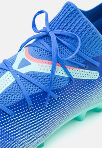 Scarpa da calcio blu con upper in maglia testurizzata e accenti a contrasto. Presenta un motivo a gradiente, lacci rotondi e una suola verde chiaro.