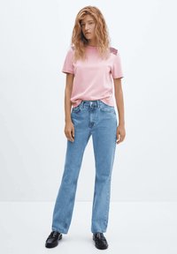 Camiseta rosa de manga corta con detalle texturizado en los hombros, combinada con vaqueros de pierna recta azul claro y mocasines negros. Tela suave, estilo casual.