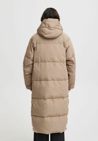 Giacca lunga imbottita beige con cappuccio, caratterizzata da cuciture orizzontali e una vestibilità comoda. Il design presenta una texture liscia e morbida.