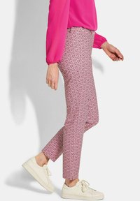 Aangestripte roze gestipte broek met een geometrisch ontwerp, gecombineerd met een felroze lange mouwtop en witte lage sneakers.