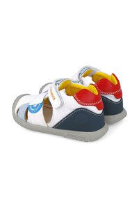 Sandali per bambini con tomaia in tela bianca, accentuazioni rosse e blu navy, fodera gialla, chiusura in velcro e suola grigia per stabilità e comfort.