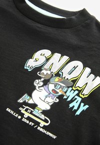 Czarna bluza z kolorową grafiką przedstawiającą kartonowego bałwana jeżdżącego na łyżwach, noszącego okulary przeciwsłoneczne, z napisem "SNOW way" i radosnymi akcentami.