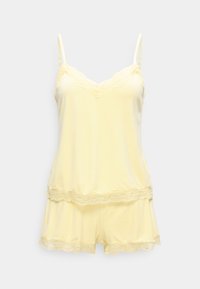 Ensemble camisole et short jaune doux avec bordure en dentelle sur le décolleté, l'ourlet et le short, présenté sur un fond uni.