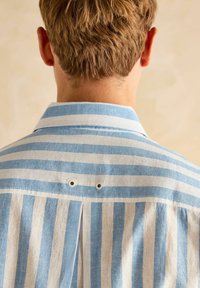 Ribaga särk, millel on sinised ja valged vertikaalsed jooned, millel on nööbid ja kaks väikest metallist silmust seljaõmbluse lähedal.