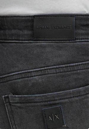 Jeans in denim nero con una finitura testurizzata, dotati di un'etichetta in pelle sulla vita che riporta la dicitura "ARMANI EXCHANGE" e un piccolo cartellino "A/X".