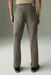 Graue Baumwolljeans mit geradem Schnitt, die über zwei Gesäßtaschen und abgesteppten Details verfügen. Der Stoff hat eine glatte Textur.