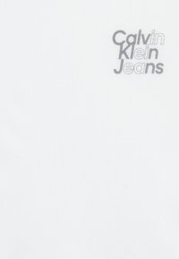 Tessuto bianco con il logo "Calvin Klein Jeans" in grigio, caratterizzato da una texture liscia e un design semplice.