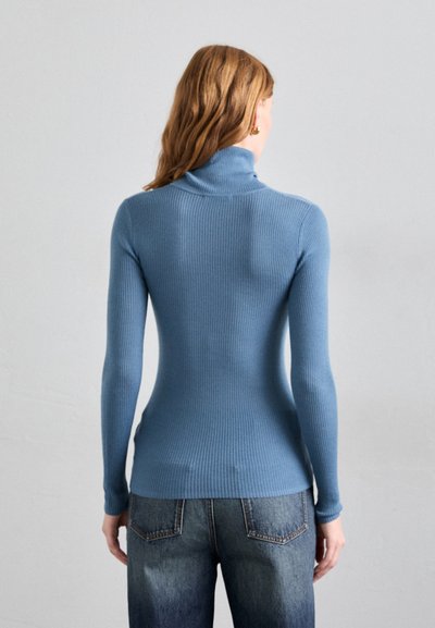 Ribbed turtleneck sweater in light blue, long sleeves, fitted shape, made of soft knit fabric. Paired with mid-rise blue jeans, minimal detailing.