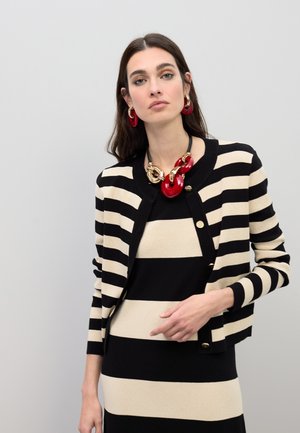 Cárdigan a rayas negras y beige con escote redondo y botones dorados, superpuesto sobre un vestido a rayas a juego. Collar y pendientes rojos llamativos.