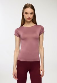 Dopasowany top z krótkim rękawem w miękkim odcieniu mauve, z okrągłym dekoltem i bezszwowym wykończeniem. Noszony z bordowymi legginsami.