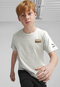 T-shirt grigio a maniche corte con colletto rotondo, caratterizzato da un logo dorato "PUMA Sports" sul petto e un logo Puma nero sulla manica.