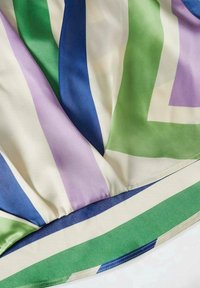 Tessuto di seta multicolore con strisce verticali in verde, viola, blu e crema, con una superficie liscia e bordo orlato.