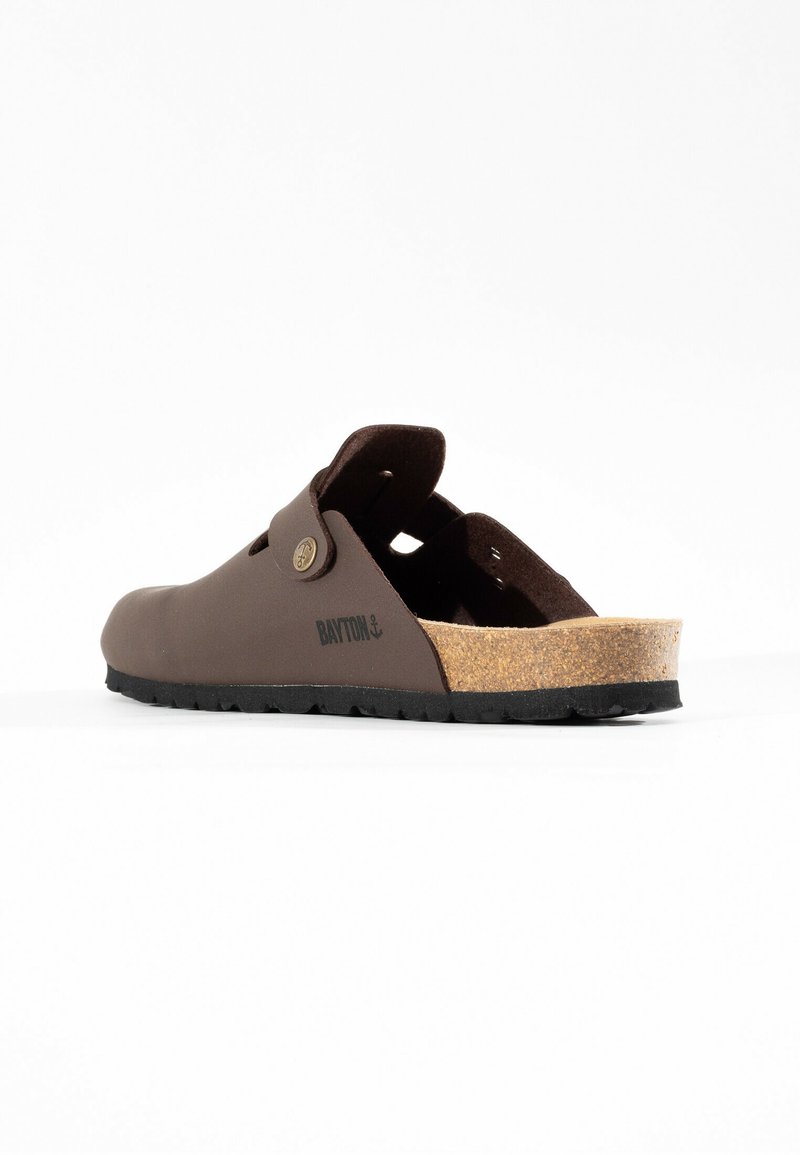 Bruine instapschoen met een kurken voetbed, rubberen zool en uitsnijdingen in het bovenwerk. Heeft een decoratieve knop en logo.