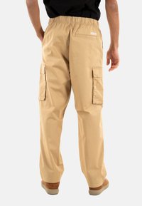 Beige cargobroek met een elastische tailleband, twee zijzakken en een achterzak. Gladde textuur en een relaxte pasvorm.